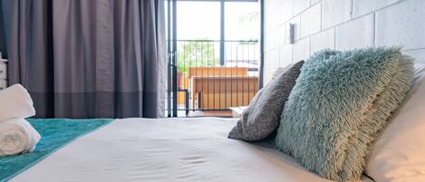 Habitación de hotel con una cama grande, vistas al balcón exterior y una cama bien hecha con una toalla blanca enrollada.