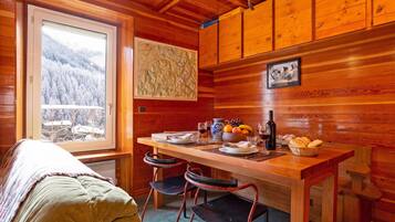 L’intérieur d’un chalet accueillant, avec un décor en bois, une table à manger mise avec des assiettes, des verres et une bouteille, et un lit recouvert d’une couverture.