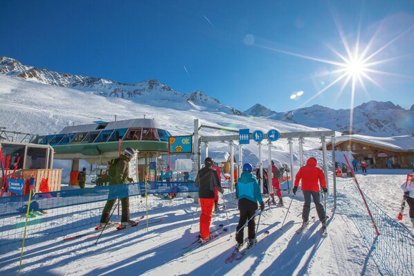 A ski resort with a snow-covered mountain backdrop, a ski lift, and a building with signage.