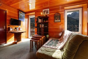Ett mysigt rum med ett träpanelat tak, en tv, en bokhylla, en soffa och ett fönster med utsikt över bergen.