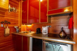 A kitchen with wooden walls, a stainless steel countertop, a coffee maker, a kettle, and a sink.