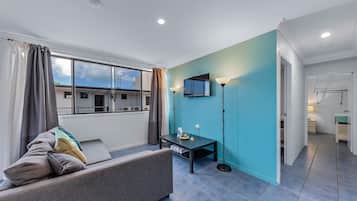 A modern living room with a sofa, a small table, a TV, and a view of the outside.