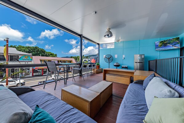A modern room with a large window, a sofa, a wooden coffee table, a small table, and a wall-mounted TV. - Airlie Sun & Sand Accommodation 6 (Airlie Beach)