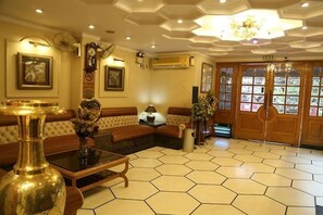 Um hall com piso hexagonal em mosaicos, um sofá, uma mesa de centro e uma porta com painéis de vidro.