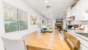 A modern kitchen with white cabinets, a wooden dining table, and a fireplace.