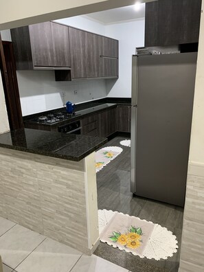 Een moderne keuken met donkere houtkasten, een zwart aanrecht en een roestvrijstalen koelkast.