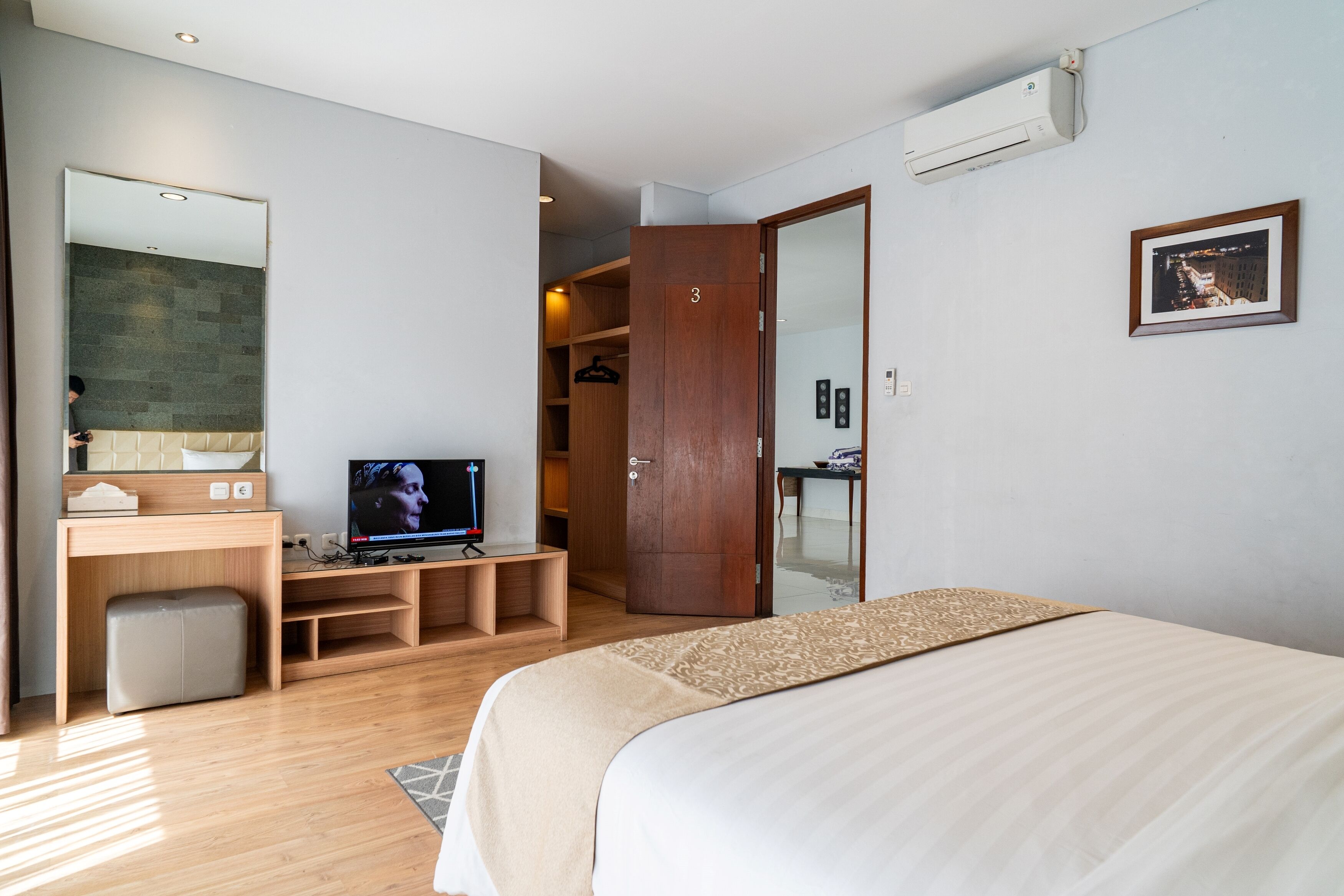A bedroom with a bed, a TV, a desk, a wardrobe, and an air conditioning unit.