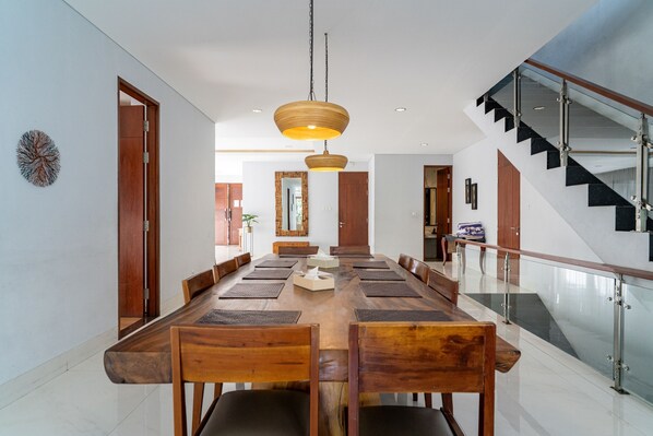 A modern dining area with a long wooden table, multiple chairs, and a hanging light fixture. - Asmaya 7BR Villa private heated pool and billiard (Cimenyan)