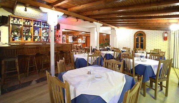 A restaurant with wooden tables and chairs, a bar area with bottles, and a brick wall. - Korali (Skiathos)