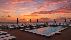 Zona junto a la piscina con sillones de descanso y sombrillas, con vista al océano al atardecer.