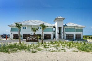 A two-story building with a beach club sign, multiple garage doors, and a clear view of the ocean.