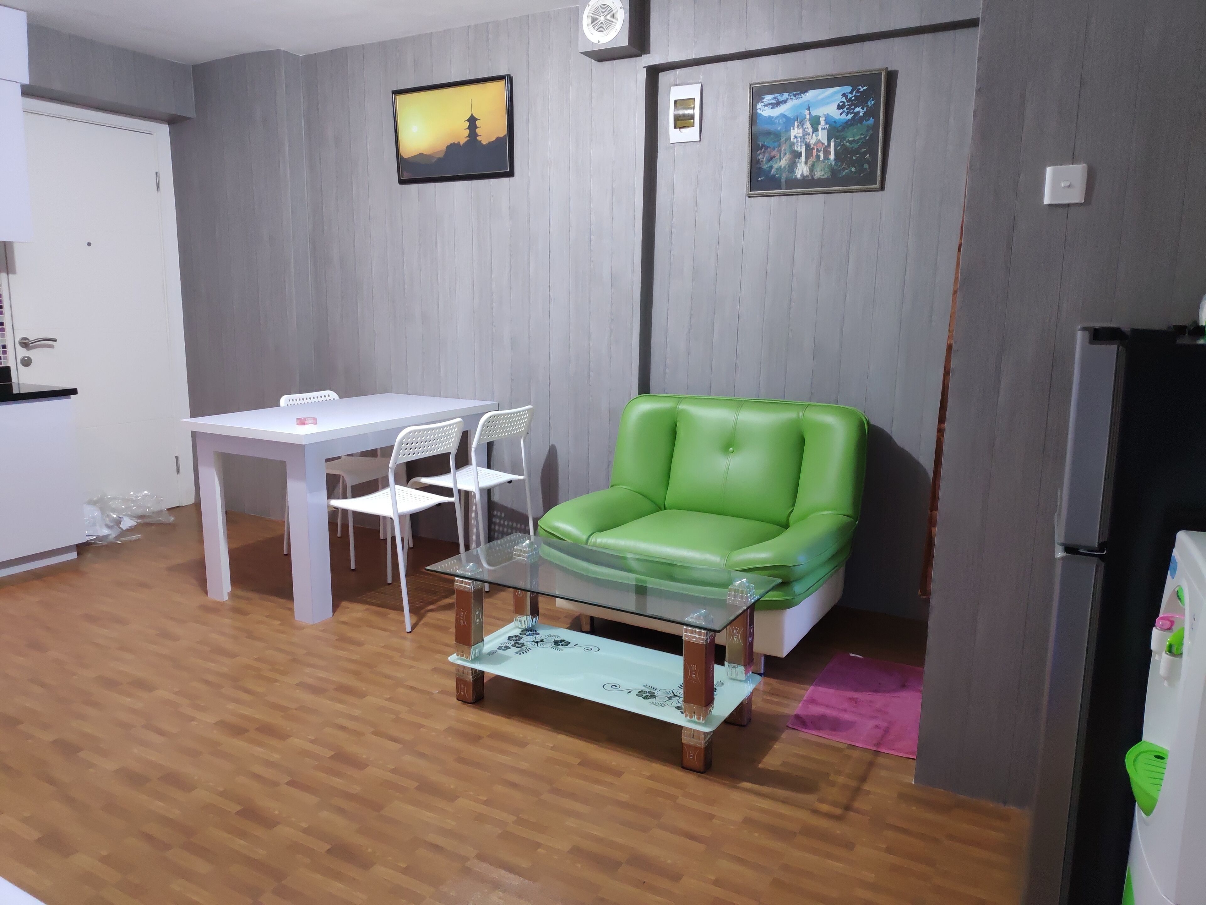 A living room with a green leather sofa, a white dining table with chairs, a glass coffee table, and two framed pictures on the wall.
