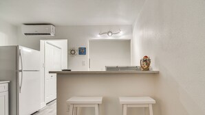 A kitchen with white cabinets, a white refrigerator, a countertop, and two white stools.