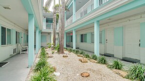 Un pasillo de hotel con paredes color turquesa, una palmera y un camino de grava.