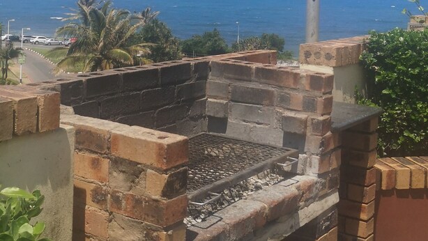 A brick barbecue grill with a clear view of the ocean and palm trees in the background. - 106 Umdloti Resort (eMdloti)