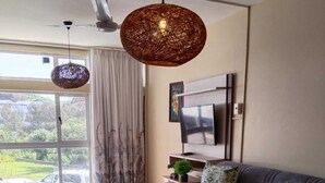 A living room with a sofa, a coffee table, a TV, and a ceiling fan. - 106 Umdloti Resort (eMdloti)