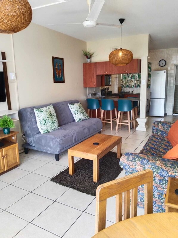 A living room with a sofa, a coffee table, and a dining area with chairs. - 106 Umdloti Resort (eMdloti)