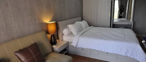 Habitación de hotel con cama, sofá, mesita de noche con lámpara y espejo.