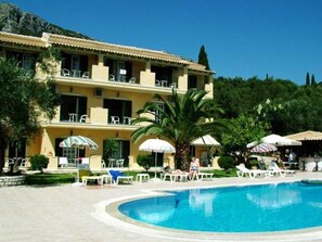 A hotel with a swimming pool, outdoor seating, and a mountainous backdrop. - Royal Rose (Corfu)