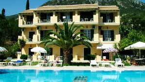 A hotel with a pool, multiple balconies, and a mountain backdrop. - Royal Rose (Corfu)