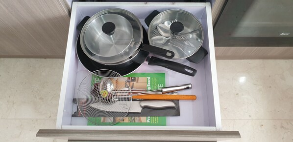 Un cajón con utensilios de cocina, incluyendo dos sartenes, una espátula, un batidor y un rallador.