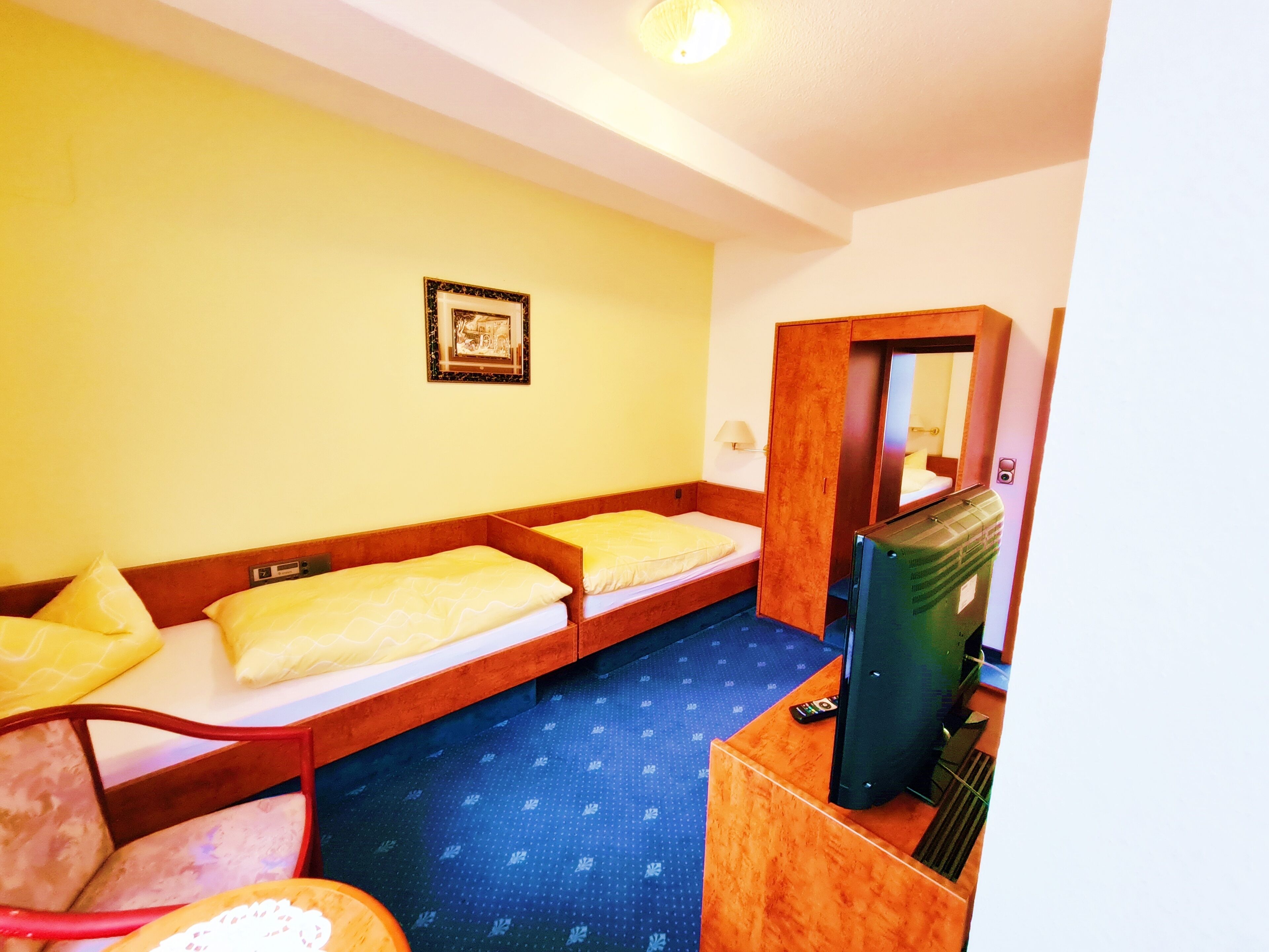 Ein Hotelzimmer mit zwei Einzelbetten, einem Schreibtisch mit Computer, einem Stuhl, einem kleinen Tisch und einem Spiegel.