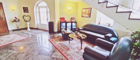 A spacious lobby with a marble floor, a black leather sofa, a coffee table, and a staircase with a railing.