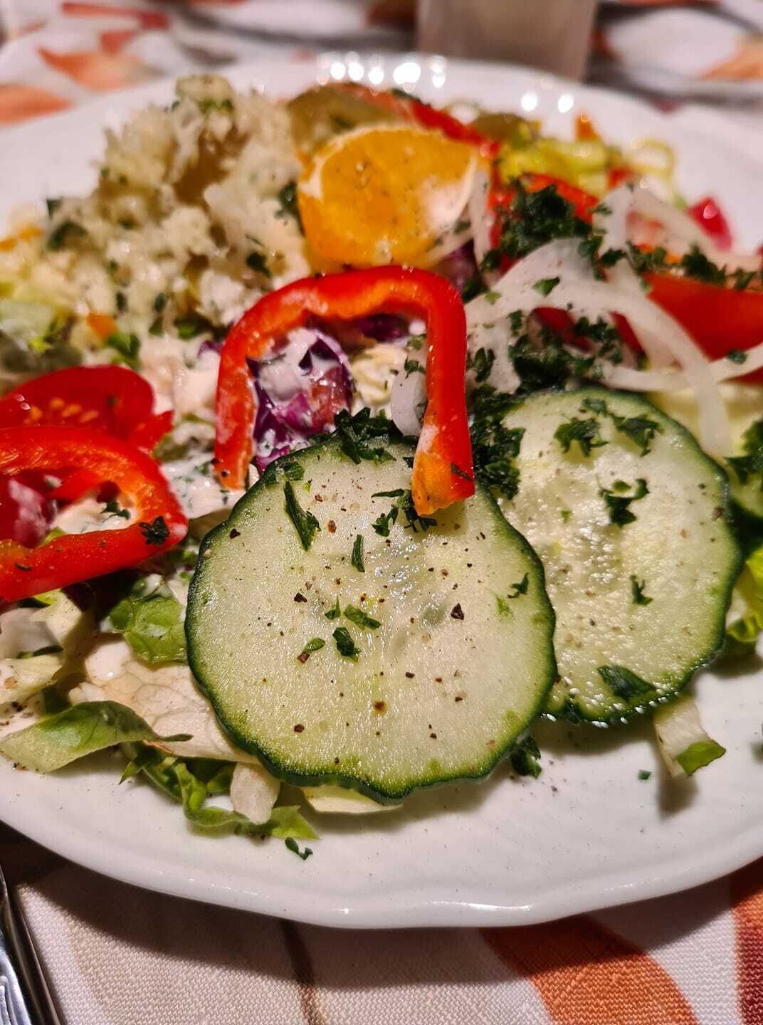 Un plato de comida con pepinos en rodajas, pimientos rojos y otras verduras.