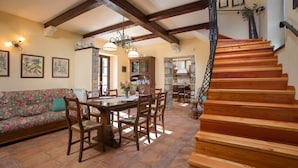 A spacious living area with a wooden staircase, a dining table with chairs, and a sofa.