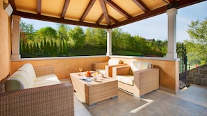 A covered outdoor seating area with wicker furniture and a view of a lush garden.