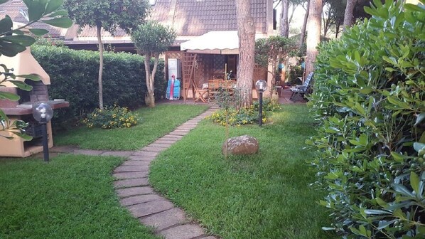 A garden with a stone pathway, a wooden table, and a covered seating area. - 200 m from the beach, 4-bed house GREEN (Calaverde Pula)
