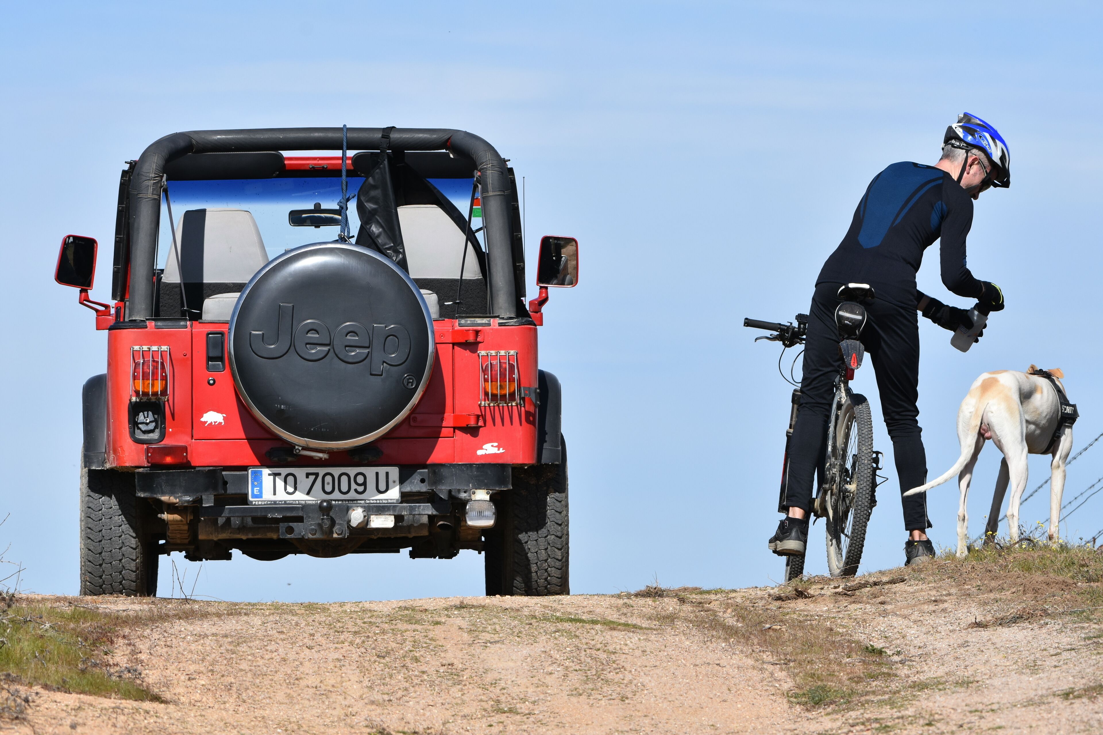 Un Jeep rouge avec une roue de secours fixée à l’arrière, garé sur un chemin de terre.