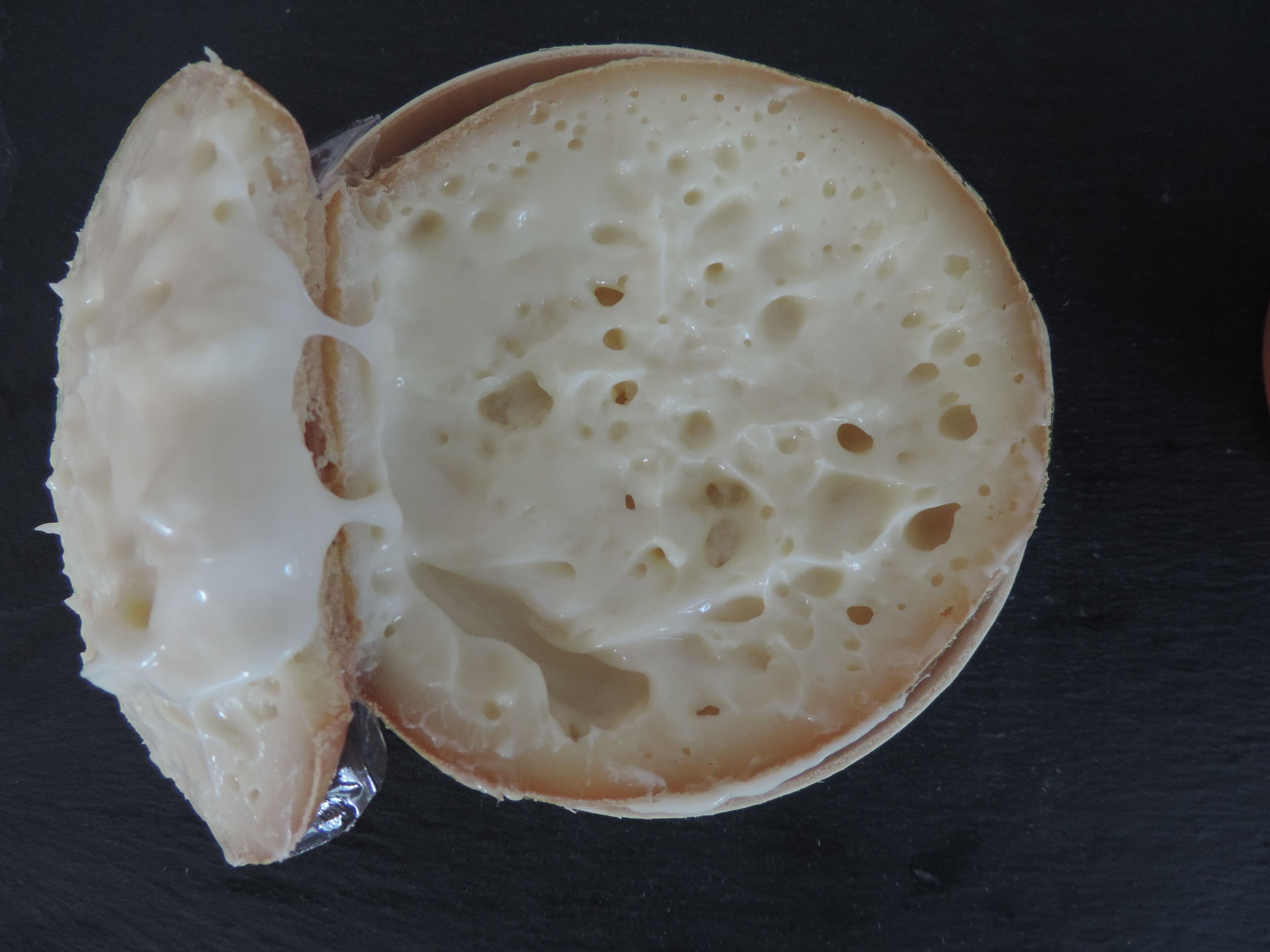 Primer plano de un pan con relleno cremoso, cortado por la mitad, sobre una superficie oscura.