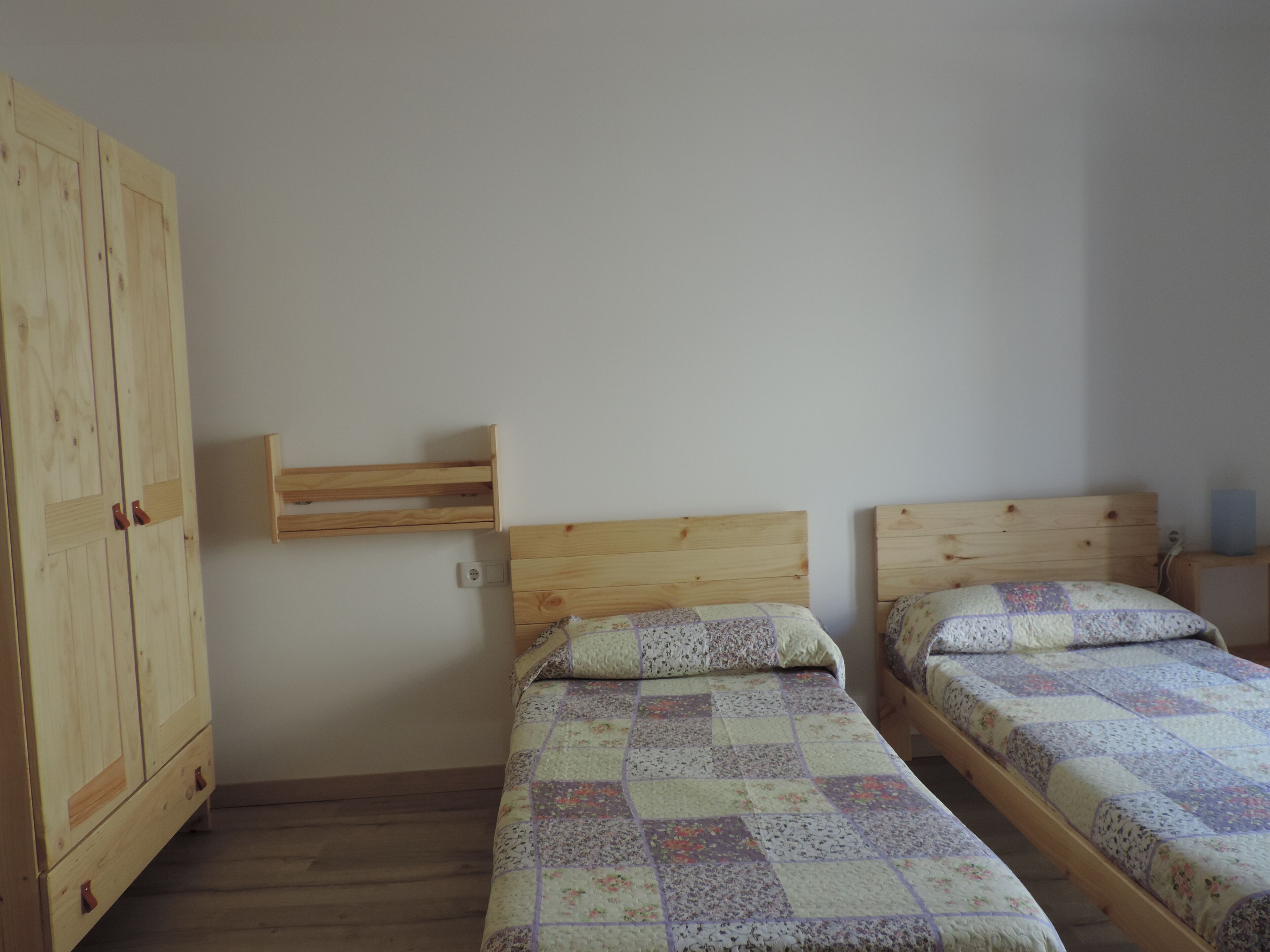 Un dormitorio con dos camas individuales, cabeceros de madera, un armario de madera y un estante pequeño.