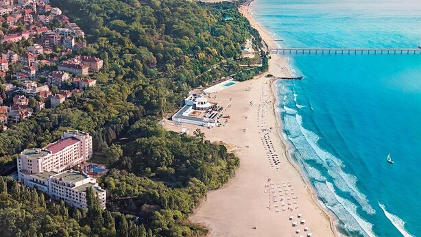 An aerial view of a coastal area with a beach, a pier, and a hotel complex.