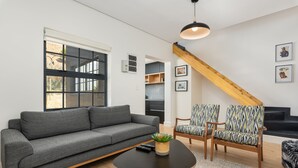 Ett modernt vardagsrum med en grå soffa, mönstrade fåtöljer, ett soffbord och en trappa med träbjälkar.
