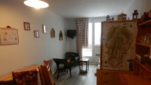 Una habitación con una mesa de comedor de madera, sillas, un televisor, un mapa en la pared y una ventana con cortinas.