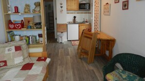 Una sala de estar acogedora con una estantería, una pequeña mesa de comedor y un sillón verde.