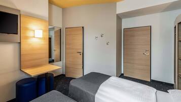 A hotel room with two beds, a TV mounted on the wall, and a wooden wardrobe.