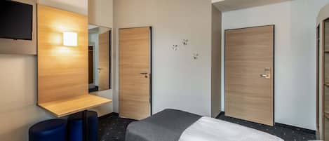 A hotel room with two beds, a TV mounted on the wall, and a wooden wardrobe.