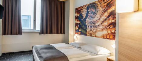 Habitación de hotel con cama, mesita de noche, escritorio, ventana con cortinas y un tapiz grande en la pared.