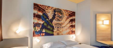 A hotel room with two beds, a large abstract painting on the wall, and a nightstand with a lamp.