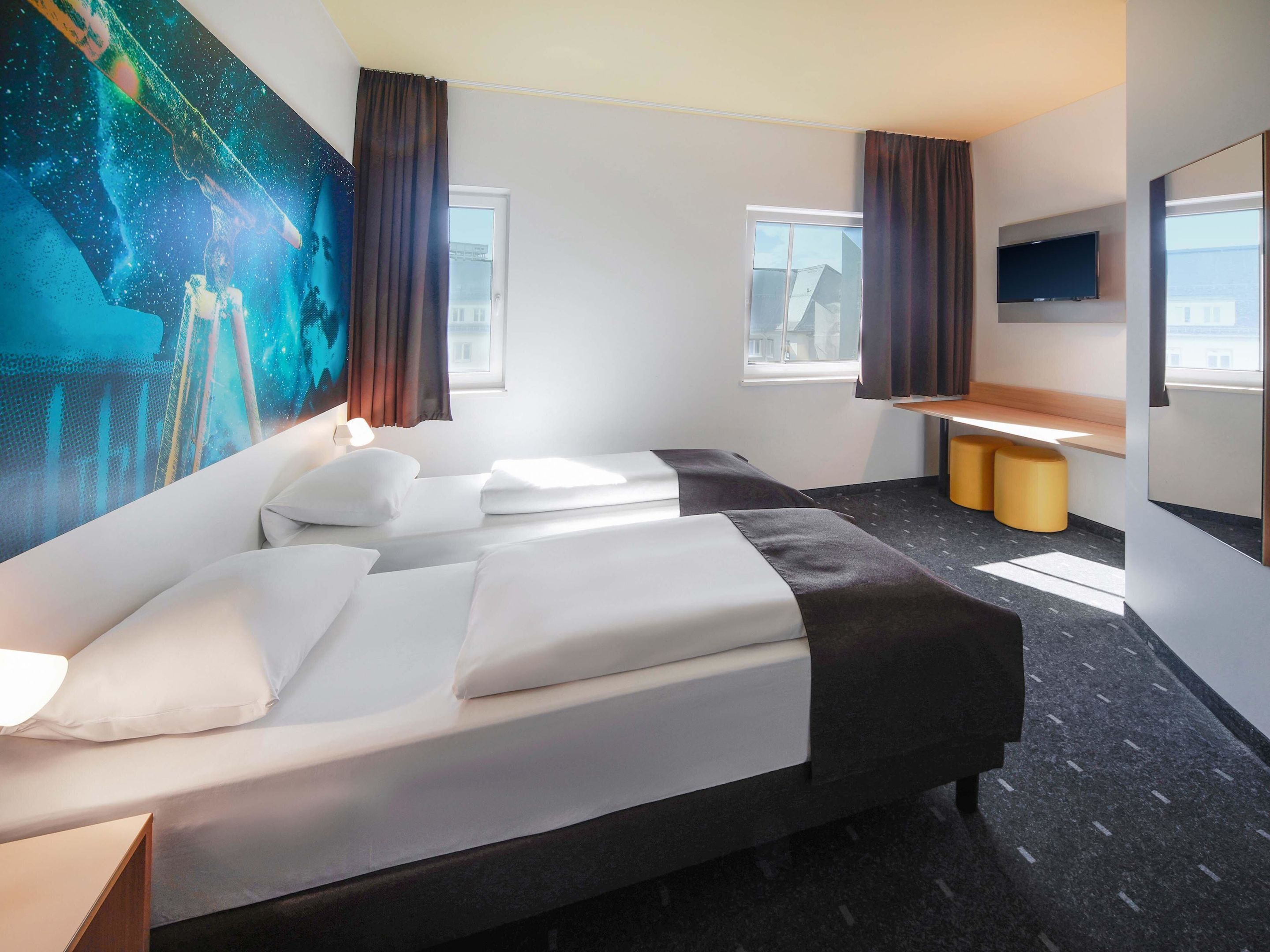 Habitación de hotel con una cama grande, un escritorio, un televisor de pantalla plana y un mural en la pared.