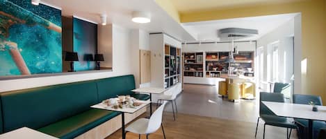 A modern cafe with a green sofa, white tables, and a starry mural on the wall.