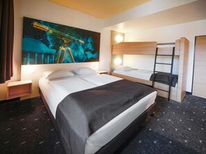 Una habitación de hotel con una cama grande, una cama más pequeña, una litera, una mesita de noche, una lámpara y un cuadro con temática espacial.