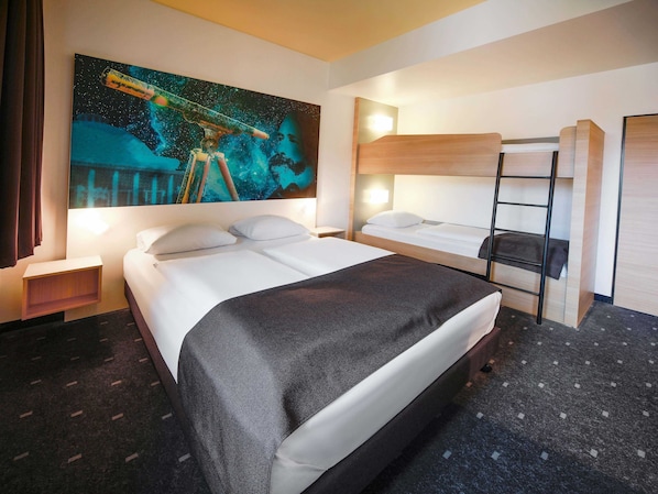 Una habitación de hotel con una cama grande, una cama más pequeña, una litera, una mesita de noche, una lámpara y un cuadro con temática espacial.