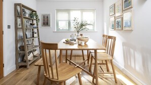A dining area with a wooden table, four chairs, a bookshelf, and a window with blinds. - Chi An Treth - sleeps 6 guests  in 3 bedrooms (Bude)