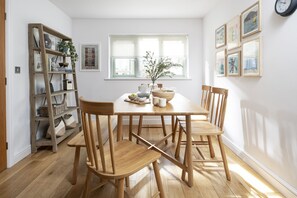 Ein Essbereich mit einem Holztisch, vier Stühlen, einem Bücherregal und einem Fenster mit Jalousien.