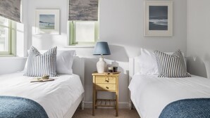 A bedroom with two beds, a nightstand, and a window with a view. - Chi An Treth - sleeps 6 guests  in 3 bedrooms (Bude)
