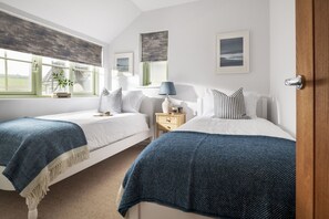 A bedroom with two beds, a nightstand, a lamp, and artwork on the walls.